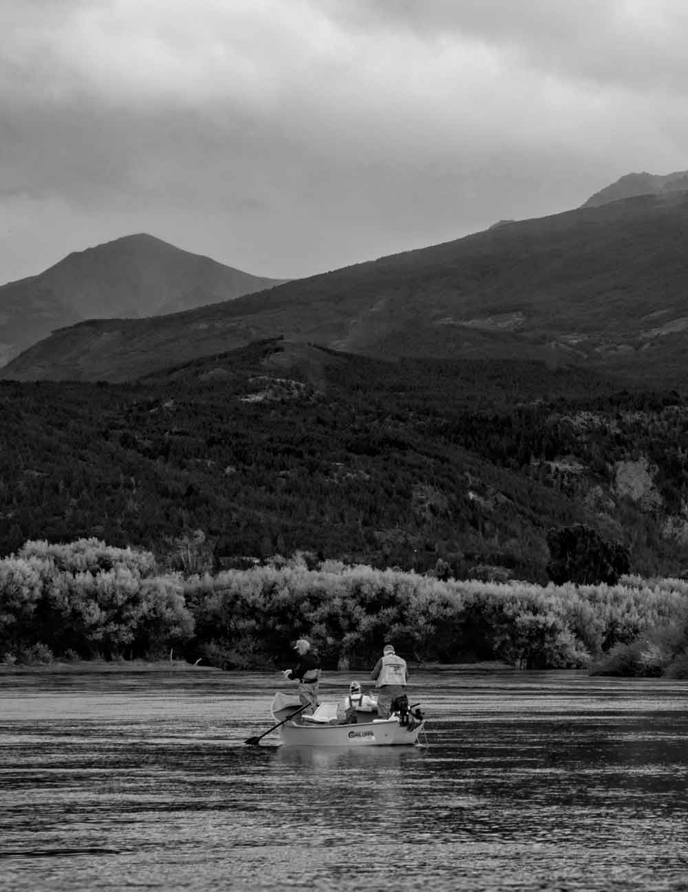 Two people in a boat on a river with mountains in the background
